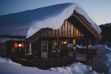 Stuga med mycket snö på taket och i vinterlandskap